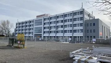 Modernes Bürogebäude mit großer Glasfassade und umliegender Baustelle unter bewölktem Himmel.