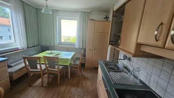 Traditionelle Küche mit Essbereich, Holzschränken und Blick ins Grüne durch die Fenster.