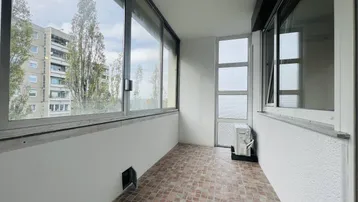 Verglaster Balkon mit Fliesenboden, Klimaanlage und Blick auf die umliegenden Gebäude.