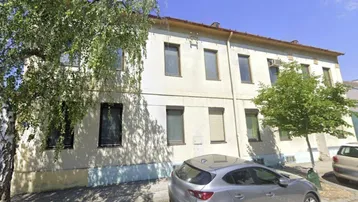 Altes Mehrfamilienhaus mit heller Fassade und Bäumen an der Straße, das Renovierungsbedarf zeigt.