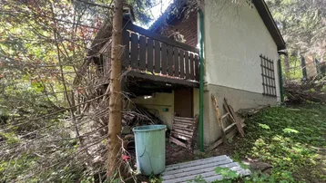 Das Haus ist von Bäumen umgeben und zeigt eine rustikale Fassade mit einem kleinen Holzbalkon.