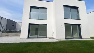Moderne weiße Hausfassade mit großen Fenstern, Schiebetüren und einer kleinen Rasenfläche.
