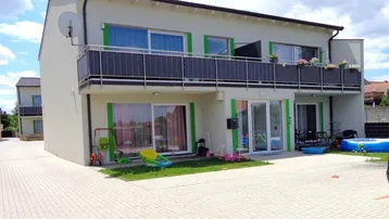 Modernes Mehrfamilienhaus mit Balkonen und gepflastertem Vorplatz unter bewölktem Himmel.