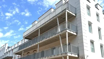 Mehrere Balkone an der Fassade eines modernen Gebäudes mit Metallgeländern unter blauem Himmel.