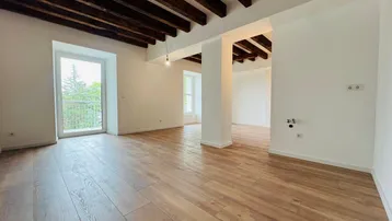 Heller Wohnraum mit Holzbalkendecke, Holzboden und Zugang zu einem französischen Balkon.