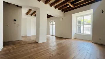 Heller, geräumiger Wohnbereich mit sichtbaren Holzbalken, neuem Holzfußboden und großen Fenstern, die viel Tageslicht hereinlassen.