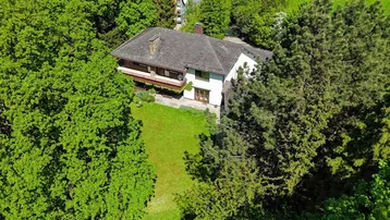 Luftaufnahme des Hauses, eingebettet in eine grüne Waldlandschaft mit altem Baumbestand.