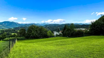 Weitläufige grüne Wiesen mit Blick auf die umliegende Berglandschaft unter blauem Himmel.