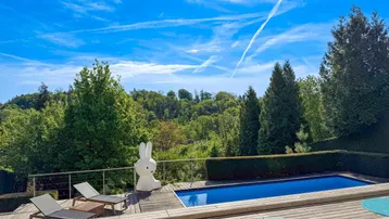 Sonniger Außenbereich mit Swimmingpool, Holzdeck und weitem Blick ins Grüne.
