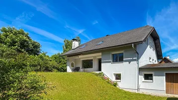 Haus mit weißer Fassade, Satteldach und grünem Garten unter blauem Himmel an einem sonnigen Tag.
