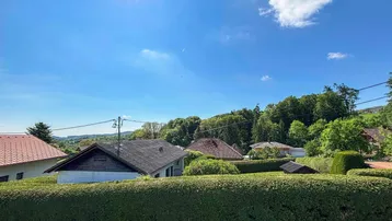 Weitblick über Dächer und grüne Hecken hinweg auf bewaldete Hügel und die umliegende Landschaft.
