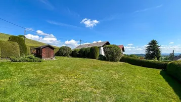 Großer, gepflegter Garten mit Rasenfläche, Hecken und einem kleinen Holzschuppen unter blauem Himmel.