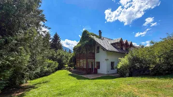 Traditionelles Haus mit üppigem Grünbewuchs an der Fassade, umgeben von einem großen Garten und Bäumen.