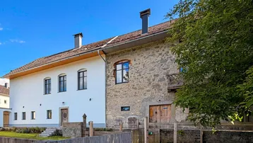 Historisches Gebäude mit weiß verputzter und steinerner Fassade unter blauem Himmel und Sonnenschein.