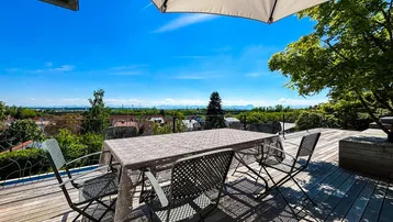 Sonnige Holzterrasse mit Esstisch und weitem Panoramablick über die Landschaft bis zu den Bergen.