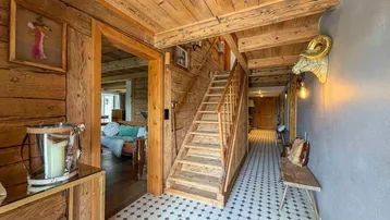 Rustikaler Flur mit Holzwänden, Holztreppe und gemusterten Fliesenboden im alpinen Stil.