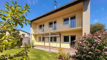 Ansicht des Hauses mit sonniger Holzterrasse, Pergola und gepflegtem Gartenbereich.