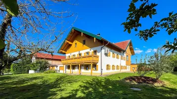 Traditionelles Haus mit Holzbalkonen und grüner Wiese unter blauem Himmel.