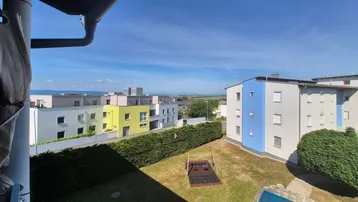 Blick von einem Balkon auf eine Wohnanlage mit Grünflächen, Spielplatz und Fernsicht.