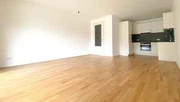Heller, offener Wohnbereich mit integrierter Küche, Parkettboden und viel natürlichem Licht.