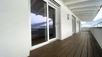 Langer Balkon mit Holzboden und Glasgeländer, bietet einen weiten Blick auf die Berge.