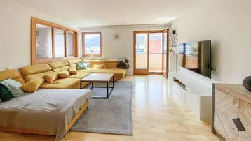 Helles Wohnzimmer mit großem Ecksofa, Holzboden und Zugang zum Balkon.