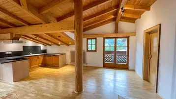 Offener Wohnbereich mit integrierter Küche, Holzbalkendecke und Zugang zu einem Balkon mit Bergblick.