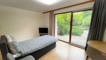 Helles Schlafzimmer mit Einzelbett, Holzboden und großen Schiebetüren zur Terrasse.