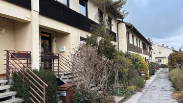Reihenhausfassade mit Eingangsbereich und gepflegter Vorgartenbepflanzung unter bewölktem Himmel.