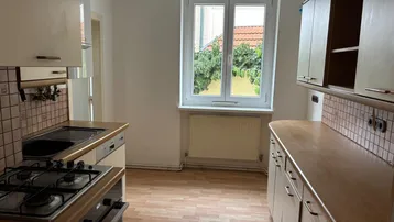 Küche mit Holzschränken, Gasherd und Fenster, das den Raum mit Tageslicht versorgt.