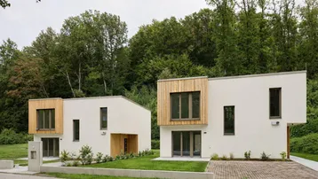 Zwei moderne Einfamilienhäuser mit Holzfassadenelementen und umgeben von viel Grün.