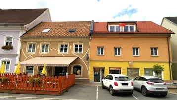 Mehrere Gebäude an einer Straße mit einem Café und Parkplätzen davor unter einem bewölkten Himmel.