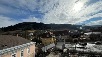 Panoramablick über die Stadt und die umliegenden bewaldeten Hügel unter einem bewölkten Himmel.