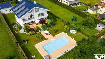 Luftaufnahme des Anwesens mit großem Pool, weitläufigem Garten und Photovoltaikanlage auf dem Dach.