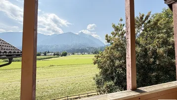 Balkon mit Holzelementen und weitem Blick auf grüne Felder und majestätische Berge.