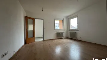 Helles, leeres Wohnzimmer mit Parkettboden und zwei Fenstern, bereit zur individuellen Gestaltung.