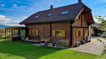 Charmantes Holzhaus mit Wintergarten und gepflegtem Rasen unter blauem Himmel.