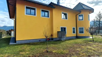 Seitenansicht des gelben Hauses mit Rasenfläche und Blick auf die Berge im Hintergrund.