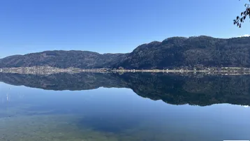 Panoramablick über den ruhigen See mit spiegelnden Bergen unter klarem blauem Himmel.