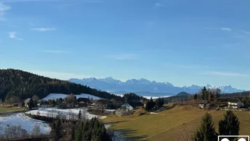 Weitläufiger Blick über eine verschneite Landschaft mit Dörfern und majestätischen Bergen im Hintergrund.