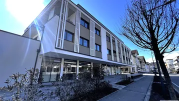 Modernes Mehrfamilienhaus mit Geschäften im Erdgeschoss und Balkonen in sonniger Lage.