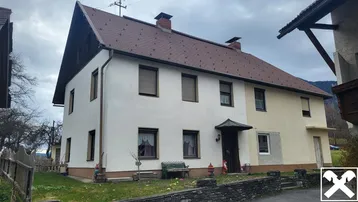 Traditionelles Wohnhaus mit Satteldach und weißer Fassade in ländlicher Umgebung.