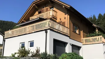 Modernes Holzhaus mit Balkonen und integrierter Garage in alpiner Umgebung.