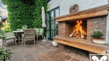 Gemütliche Terrasse mit Außenkamin, Gartenmöbeln und üppiger grüner Bepflanzung.