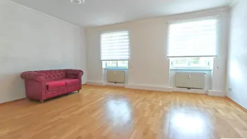 Helles Wohnzimmer mit Parkettboden, weiß gestrichenen Wänden und einem roten Sofa.
