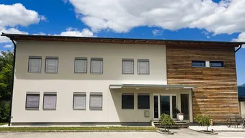 Modernes Gebäude mit heller Fassade und Holzverkleidung unter blauem Himmel und Wolken.