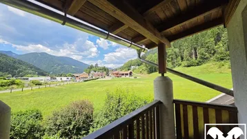 Überdachter Balkon mit Holzelementen und weitem Blick über grüne Felder und Berge.