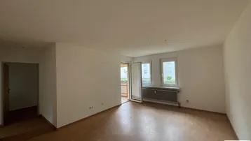 Helles, leeres Wohnzimmer mit Laminatboden und Zugang zu einem Balkon.