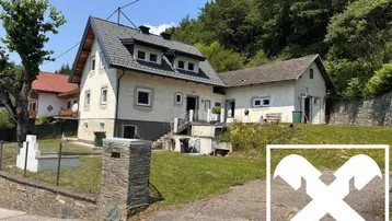 Ländliches Haus mit Satteldach und großem Vorgarten, umgeben von grüner Natur.