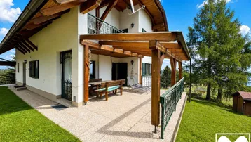 Große gepflasterte Terrasse mit Holzpergola, Gartenmöbeln und weitem Blick auf die umliegende Landschaft.